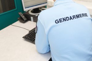 gendarme homme en uniforme assis devant un bureau avec un ordinateur et un clavier posés sur la table