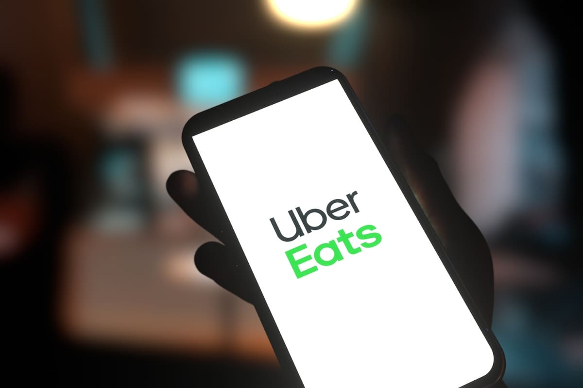 Main tenant un smartphone avec l'écran affichant le logo Uber Eats 
