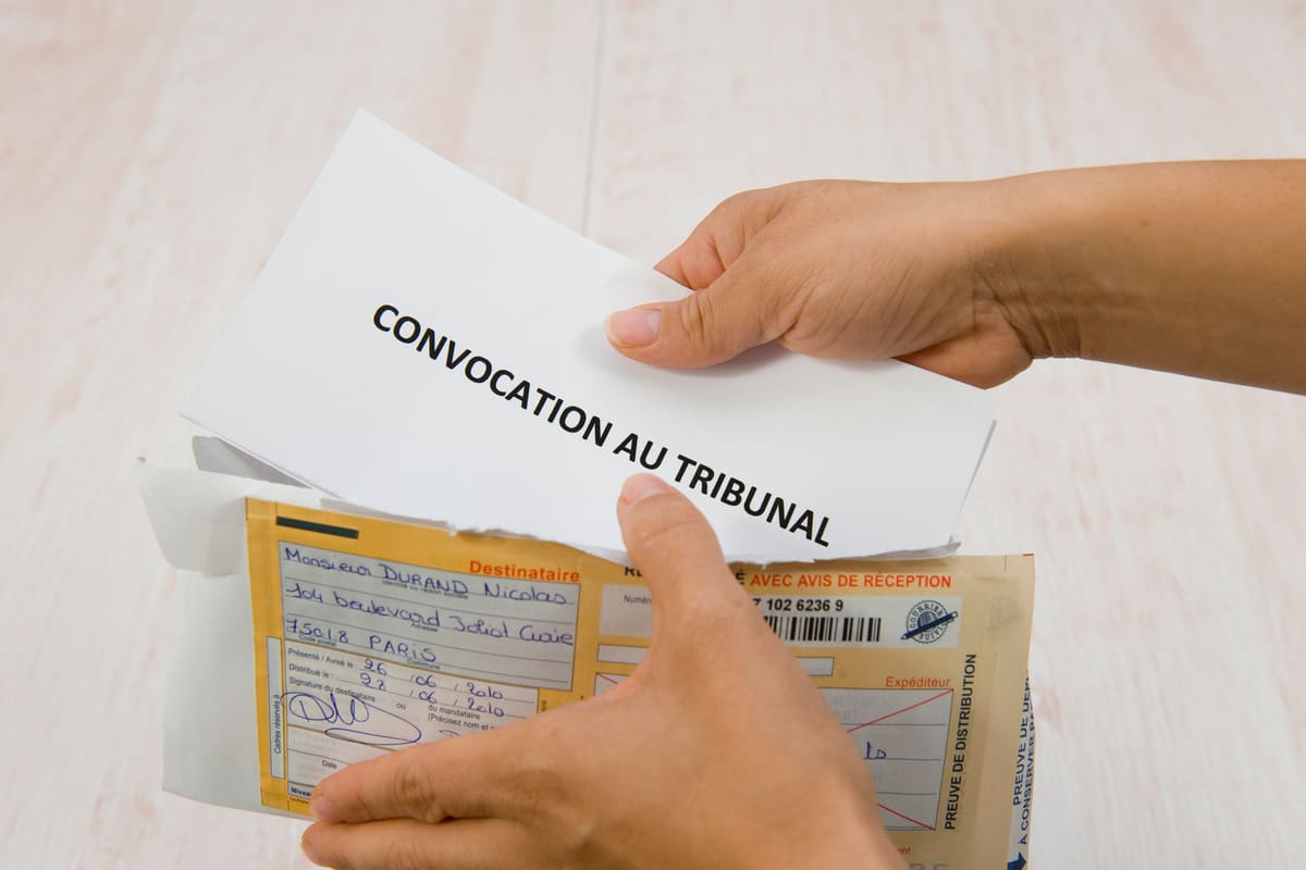 main faisant sortir d'une enveloppe une feuille blanche avec inscription convocation au tribunal 